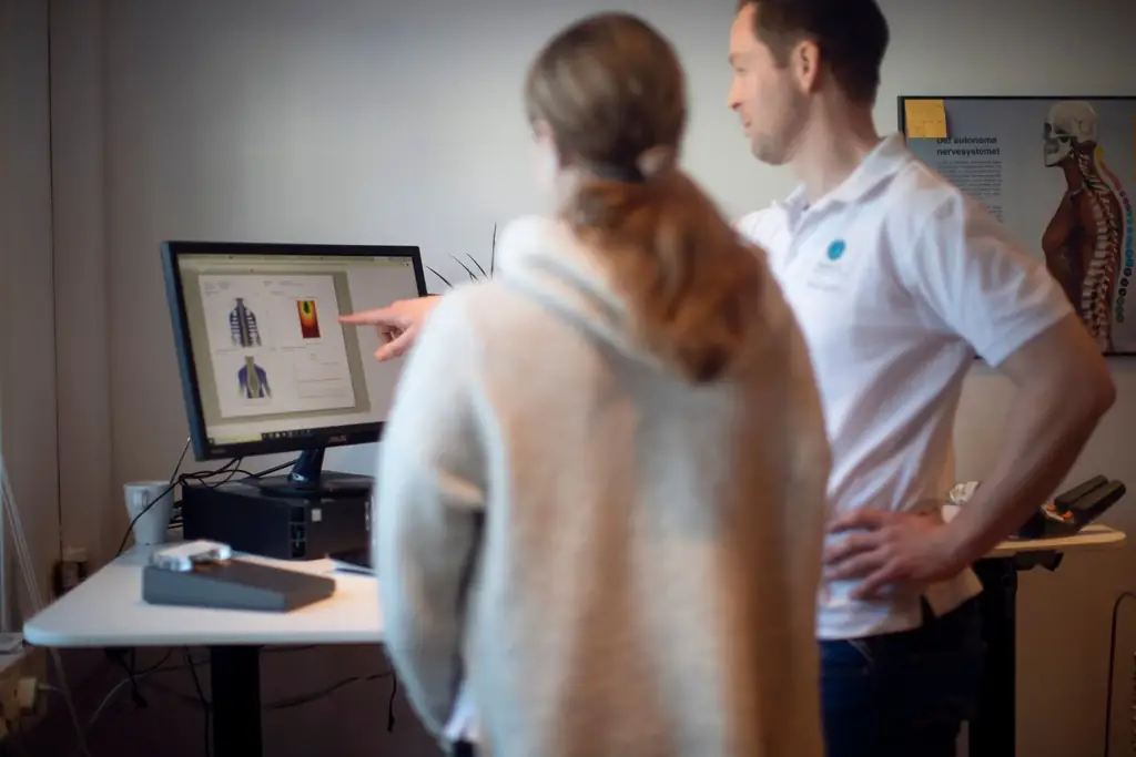CLA Scanning. En person og helsepersonell ser på en dataskjerm som viser diagrammer av menneskekroppen; innendørs setting.